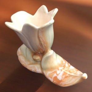 May include: A ceramic tulip-shaped vase with a marbled glaze in shades of white, green, and orange. The vase is designed to look like a tulip flower with a single leaf.