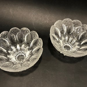 以下が含まれることがあります： 装飾的な波状の縁と花柄が施された、透明なガラス製のボウルが2つ。ボウルは空で、光沢のある仕上げになっています。