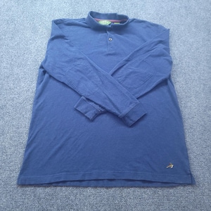Puede incluir: Un polo azul de manga larga con cuello, una tapeta de un solo botón y parches reforzados en los codos. La prenda incluye un pequeño logotipo bordado en la parte inferior delantera y una etiqueta de la marca Orvis en el cuello.