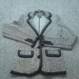 May include: A black and white speckled blazer featuring a notched lapel, long sleeves with three decorative buttons on each cuff, and two front pockets. The garment is accented with black trim along the lapels, cuffs, pockets, and front closure.