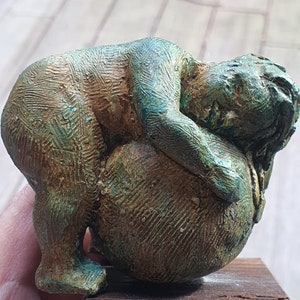 Könnte beinhalten: Eine Bronzeskulptur eines schlafenden Kindes auf einem runden Objekt. Die Skulptur hat eine grüne Patina und wird auf einem Holzsockel präsentiert.