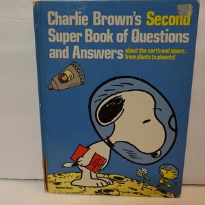 May include: A blue hardcover book titled Charlie Brown's Second Super Book of Questions and Answers about the earth and space... from plants to planets! The cover features Snoopy in a space helmet on the moon with Woodstock and a space capsule.