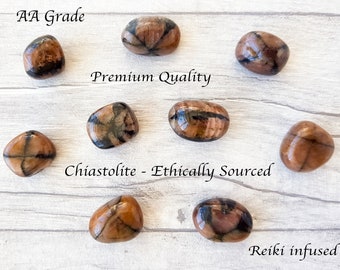 Puede incluir: Varias piedras de Chiastolita de grado AA, de origen ético e infundidas con Reiki. Estas piedras pulidas son marrones con un patrón en forma de cruz. La imagen muestra varias piedras sobre una superficie clara con vetas de madera.