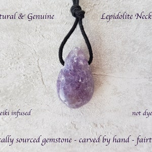Puede incluir: Un collar de lepidolita natural con una gema p&uacute;rpura en forma de l&aacute;grima. El collar cuelga de un cord&oacute;n negro. El texto en la imagen dice: "Natural & Genuine", "Lepidolite Necklace", "Reiki infused", "not dyed" y "ethically sourced gemstone - carved by hand - fairtrade".