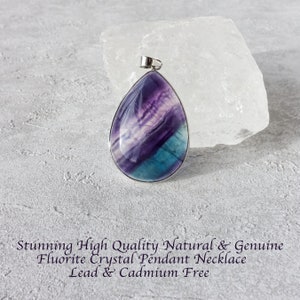 May include: A teardrop-shaped fluorite crystal pendant with a silver bail. The pendant displays a mix of purple, white, and teal hues. The image text reads: "Stunning High Quality Natural & Genuine Fluorite Crystal Pendant Necklace Lead & Cadmium Free."