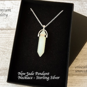 Könnte beinhalten: Eine hellgrüne Jade-Anhänger-Halskette in einer schwarzen Geschenkbox. Der Anhänger hat eine sechseckige Form mit einer Silberkette. Der Text "New Jade Pendant Necklace - Sterling Silver" ist sichtbar. Die Wörter "Premium Quality" und "ethically sourced" sind ebenfalls sichtbar.