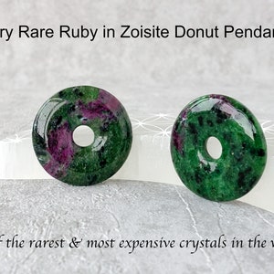 Könnte beinhalten: Zwei polierte Anhänger in Donutform. Die Anhänger sind eine Mischung aus Grün und Rubinrot. Der Text oben lautet "Very Rare Ruby in Zoisite Donut Pendants". Der Text unten lautet "one of the rarest & most expensive crystals in the world".