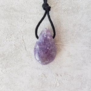 Puede incluir: Colgante de amatista morada en forma de l&aacute;grima con cord&oacute;n negro. La piedra pulida muestra tonos p&uacute;rpuras. El cord&oacute;n negro anudado crea un dise&ntilde;o sencillo y elegante para esta joya.