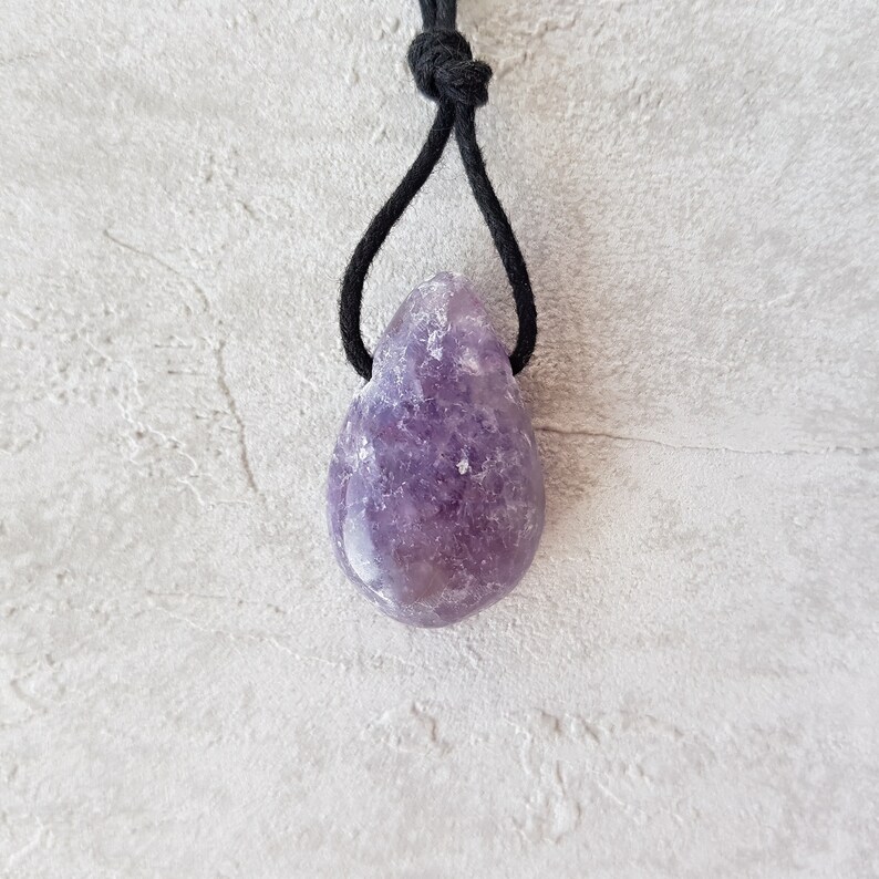 Puede incluir: Colgante de amatista morada en forma de l&aacute;grima con cord&oacute;n negro. La piedra pulida muestra tonos p&uacute;rpuras. El cord&oacute;n negro anudado crea un dise&ntilde;o sencillo y elegante para esta joya.