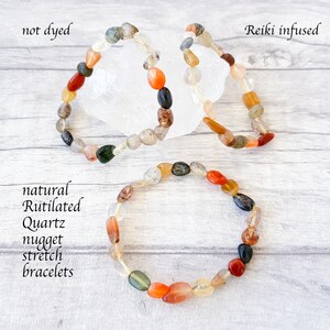 May include: Three natural Rutilated Quartz nugget stretch bracelets. The bracelets are made of various colors of quartz, including clear, orange, red, green, and black. The text "not dyed" and "Reiki infused" are visible.