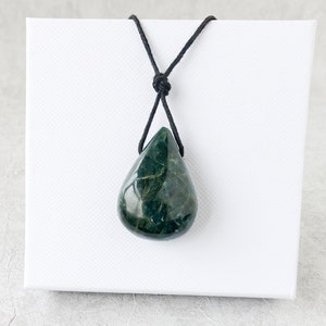 May include: A dark green, teardrop-shaped pendant necklace. The polished stone is suspended from a black cord, knotted at the top. The pendant is displayed against a white square background.