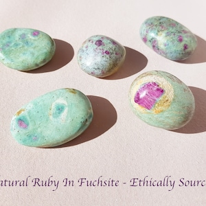 May include: Five polished natural ruby in fuchsite stones. The stones are oval and round, with a light green base colour and pink and red ruby inclusions. The text "Natural Ruby In Fuchsite - Ethically Sourced" is at the bottom of the image.