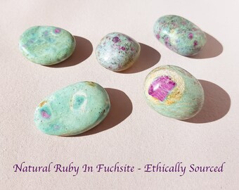 Puede incluir: Cinco piedras pulidas de rubí natural en fucsita. Las piedras son ovaladas y redondas, con un color base verde claro e inclusiones de rubí rosa y rojo. El texto "Natural Ruby In Fuchsite - Ethically Sourced" está en la parte inferior de la imagen.