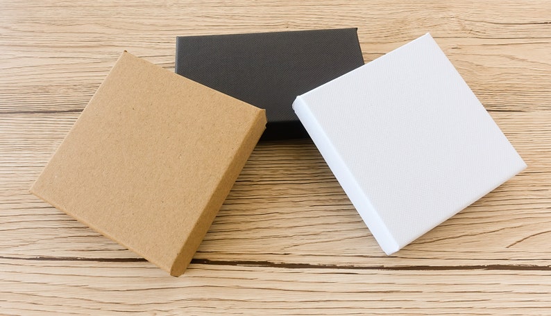 Puede incluir: Tres cajas cuadradas de diferentes colores est&aacute;n dispuestas sobre una superficie de madera marr&oacute;n claro. Las cajas son de color marr&oacute;n natural, negro y blanco. Las cajas est&aacute;n cerradas y parecen vac&iacute;as.