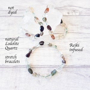 May include: Three natural Lodolite Quartz stretch bracelets. The bracelets feature a variety of colorful, oval-shaped beads in shades of clear, green, brown, and black. The text on the image reads "not dyed" and "Reiki infused."