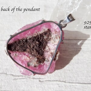 May include: A pendant with a pink and brown stone, set in a silver frame. The back of the pendant is visible, with the text "the back of the pendant" and "925 stamped". The stone has a rough, natural texture.