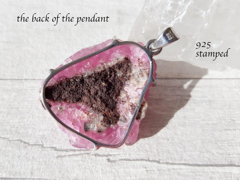 May include: A pendant with a pink and brown stone, set in a silver frame. The back of the pendant is visible, with the text "the back of the pendant" and "925 stamped". The stone has a rough, natural texture.