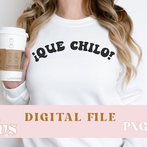 May include: White sweatshirt with the text "¡QUE CHILO!" in black retro-style lettering. The sweatshirt is being worn by a person holding a coffee cup.