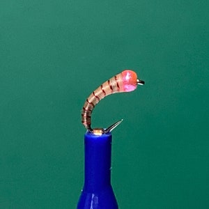 May include: A pink and brown fly fishing lure with a hook.