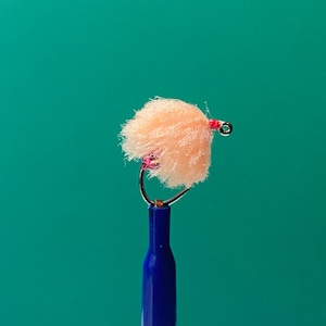 May include: A peach-colored fly tying material tied to a hook with a pink bead and red thread.