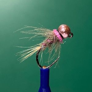 May include: A pink and brown fly fishing lure with a copper bead head and a brown and white feather tail.