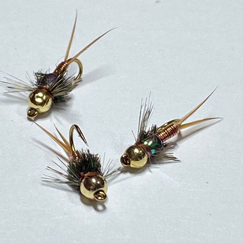 May include: Three gold-headed fly fishing lures with brown, green, and iridescent wings. The lures have copper wire bodies.