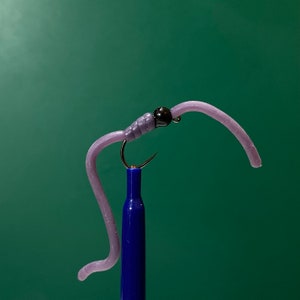 May include: A purple rubber worm fly fishing lure with a black bead head.