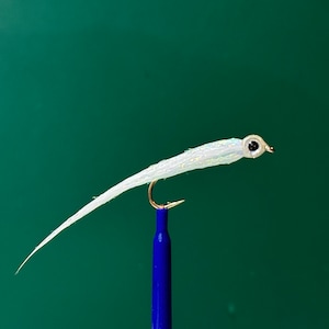 May include: A white fly fishing lure with a realistic eye and a long, thin body. The lure is tied to a blue hook.