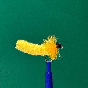 May include: A yellow and brown fly fishing lure with a fuzzy body and a bead head.