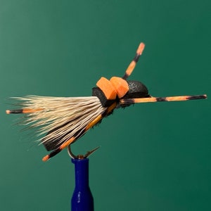 May include: A black and orange fly fishing lure with a white feather tail and orange foam body.