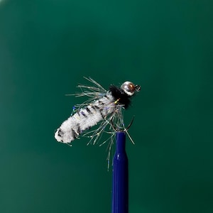 May include: A black and white fly fishing lure with a silver bead head and iridescent fibers. The lure is mounted on a blue rod.
