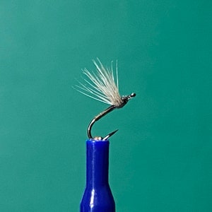 Può includere: Un'esca da pesca a mosca bianca e grigia con un amo argentato, legato a una canna da pesca blu.