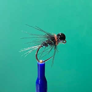 Puede incluir: Un señuelo de pesca con mosca negro y verde con una cabeza de cuentas negras y una cola de plumas blancas.
