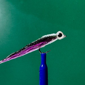 May include: A purple and black fly fishing lure with white and silver accents and a black eye. The lure is mounted on a blue fishing rod.