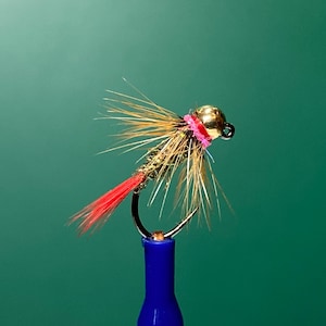 May include: A gold and pink fly fishing lure with a red tail, tied on a blue hook holder.