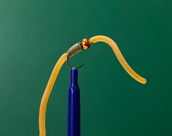 May include: A tan worm-shaped fly fishing lure with a gold bead and a hook. The lure is attached to a blue fishing rod.