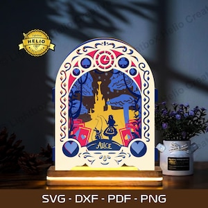 May include: A decorative, layered light featuring an Alice in Wonderland design. The artwork includes silhouettes of Alice, the White Rabbit, and a castle, with playing card symbols. The base is a wooden stand with a warm glow. The text "ALICE" is visible.