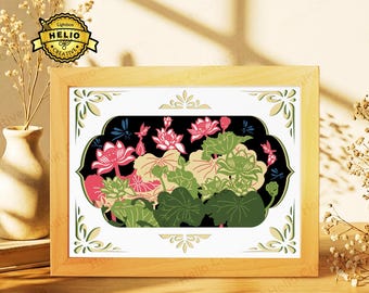 May include: A rectangular wooden frame containing a layered paper-cut art piece featuring pink lotus flowers, green lily pads, and small blue dragonflies against a black background, with decorative cream-colored corner accents on a white border.