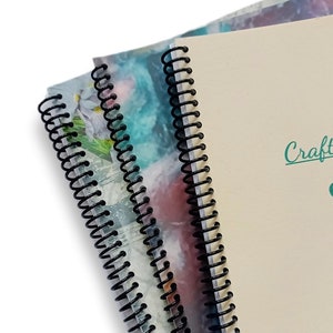 May include: Three notebooks with black wire-o binding. The front cover of the notebook on the right has the text "Craft" in teal green.