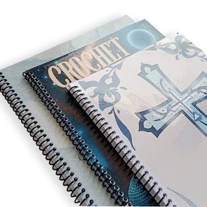 May include: Three spiral-bound notebooks with glossy covers. The top notebook has a light blue cover, the middle one has the word "CROCHET" on it, and the bottom one has a cross design. The notebooks are stacked at an angle.
