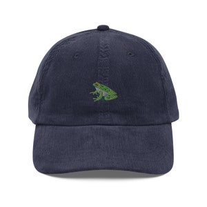 Könnte beinhalten: Eine marineblaue Baseballkappe aus Cord mit einer gestickten grünen Frosch mit roten Augen.