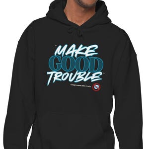 Può includere: Felpa con cappuccio nera con la scritta "MAKE GOOD TROUBLE" in turchese e bianco. Il testo ha un effetto ombra. La felpa è indossata da una persona. Ha un cappuccio con coulisse e una tasca frontale. Il testo è in un carattere stilizzato.