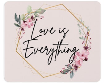 Peut inclure: Un tapis de souris rectangulaire sur fond rose clair avec le texte noir "Love is Everything." Un cadre hexagonal géométrique doré entoure le texte, agrémenté de fleurs de cerisier roses et de feuilles vertes style aquarelle.
