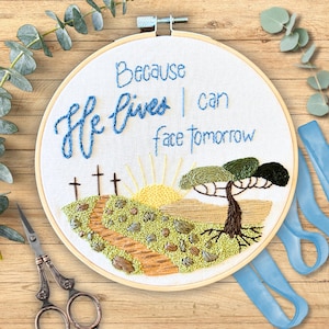May include: Embroidered hoop art with a sunrise, a path, and three crosses. The text reads "Because He lives I can face tomorrow".