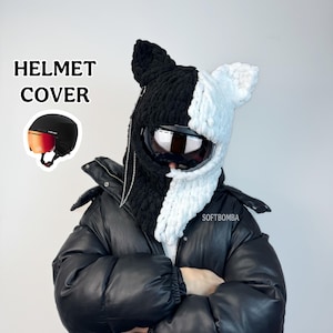 May include: A black and white knitted helmet cover with a cat ear design. The cover has a built-in visor and a chain detail. The words "HELMET COVER" are printed on the left side of the image.