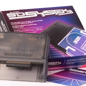 Pode incluir: Uma unidade de CD-ROM Super System 3 preta para o Super Nintendo Entertainment System (SNES). A unidade é mostrada com sua embalagem, que apresenta um padrão de grade roxo e azul e o texto "SUPER SYSTEM 3".