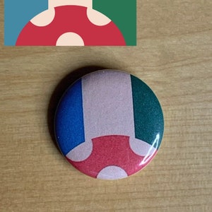 May include: A round button with a mushroom design. The mushroom is red with white spots and is on a background of blue, pink, and green.