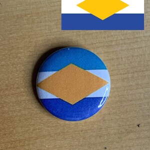 May include: A blue, white, and yellow button with a diamond shape in the center. The button is a representation of a flag.