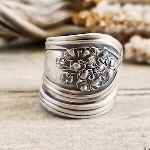 May include: A silver spoon ring with a floral design. The ring is made from a vintage spoon and has been hammered and polished to give it a unique look.