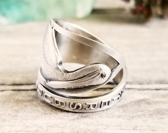 Puede incluir: Un anillo de plata hecho de una cuchara reutilizada con un diseño de pájaro y las palabras "In God We Trust" grabadas en la banda.